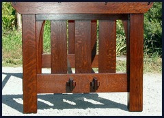 View of the end of the table showing the pinned through-tenons on the legs, the keyed through-tenons on the lower stretcher and the arched corbels framing the slats.